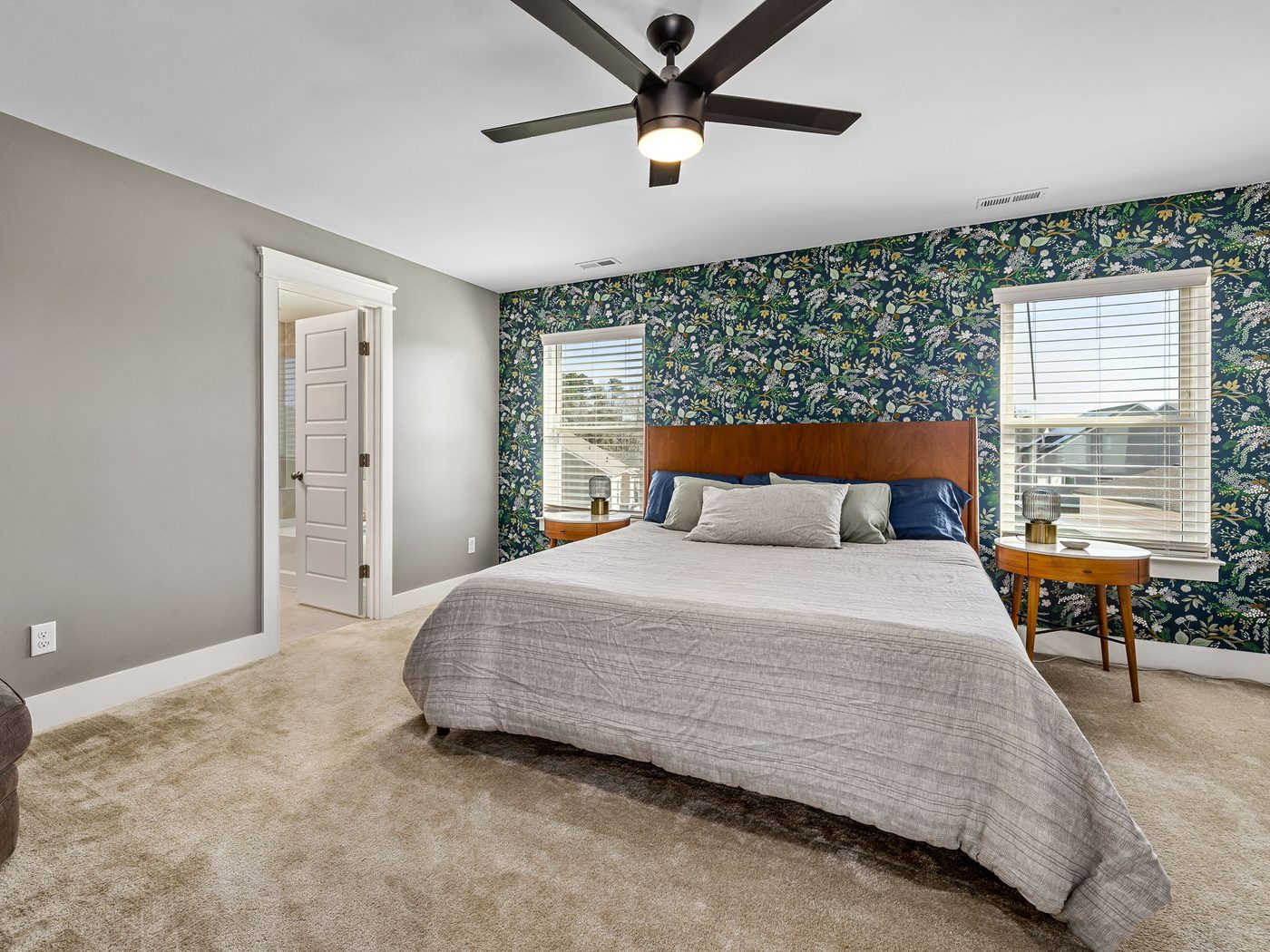 Bedroom with a dark green botanical wallpaper accent wall behind a wood headboard, gray walls and a ceiling fan
