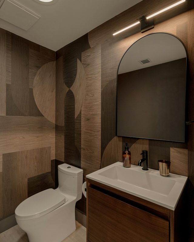 Contemporary powder room with a geometric wood-look wallcovering, an arched black-framed mirror and a floating vanity