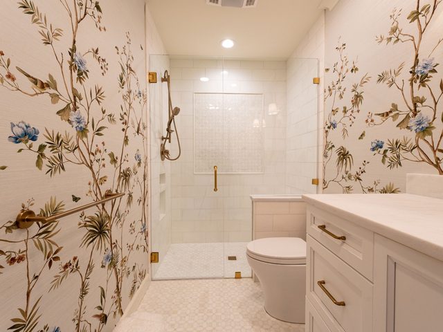 Light bathroom with cream wallpaper of flowering branches and birds, a white vanity and brass fixtures
