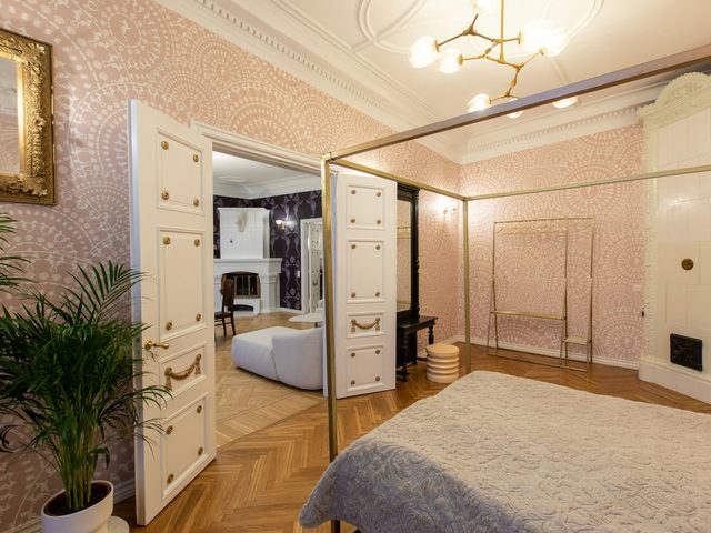 Elegant bedroom with blush lace-medallion wallpaper, a brass four-poster bed and white paneled doors