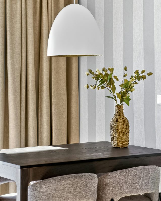 Modern dining nook with wide gray and white striped wallpaper, a white pendant light and a vase of branches on a dark table