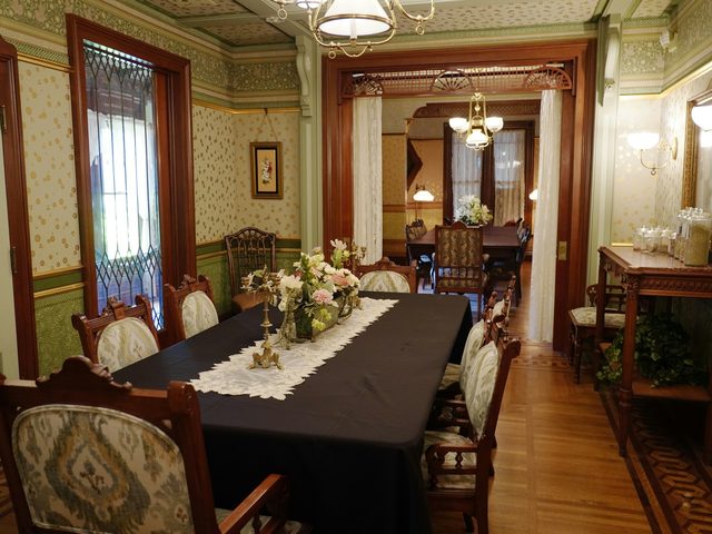 Traditional dining room with small floral wallpaper, a green frieze, oak trim and a chandelier over a long table
