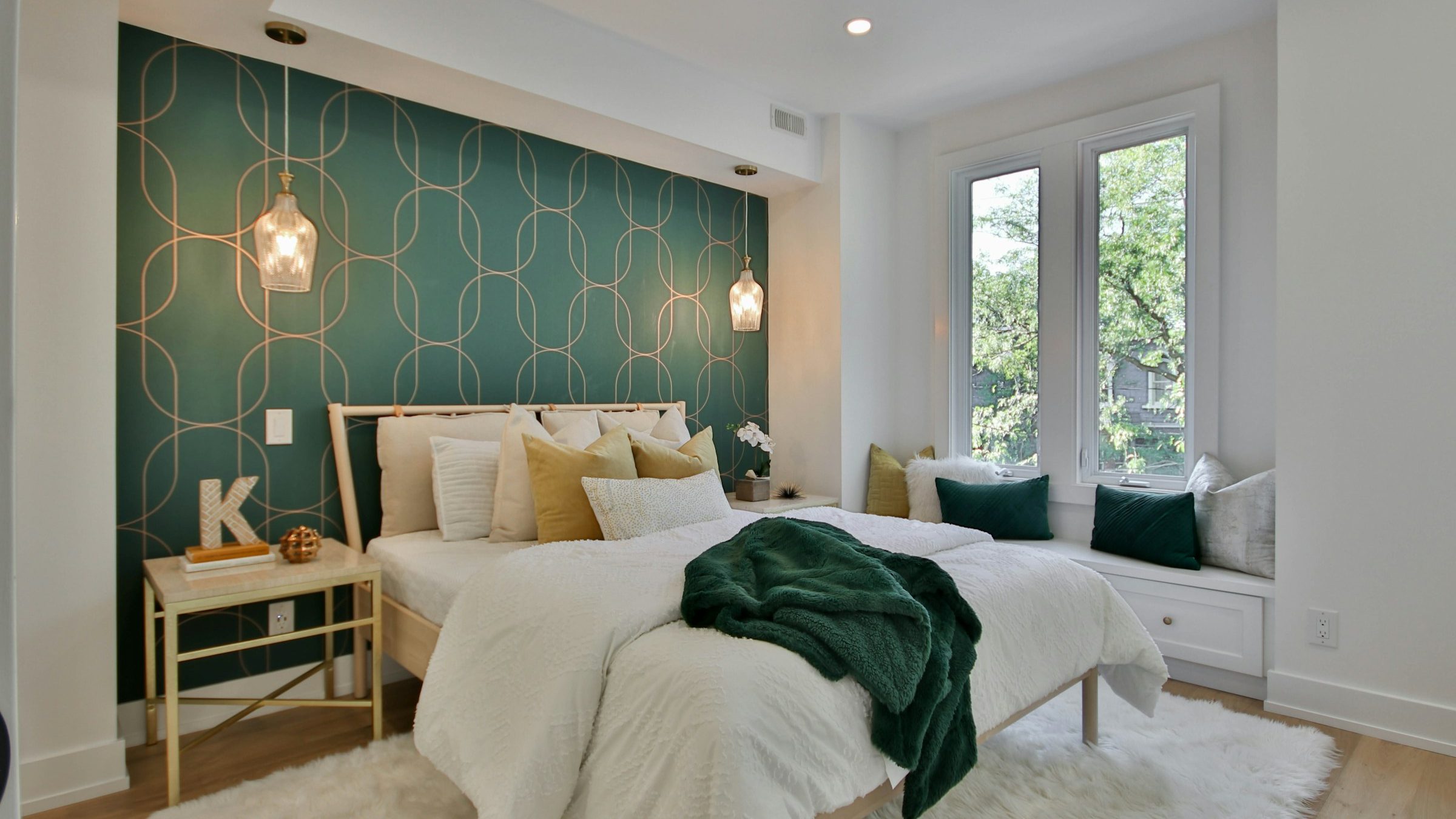 Bright bedroom with a deep green and gold arch-pattern wallpaper accent wall behind the bed, glass pendant lights and white linens