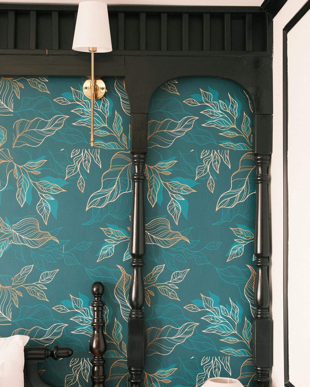 Close-up of teal wallpaper with gold leaf outlines set inside black arched millwork, with a brass wall sconce above